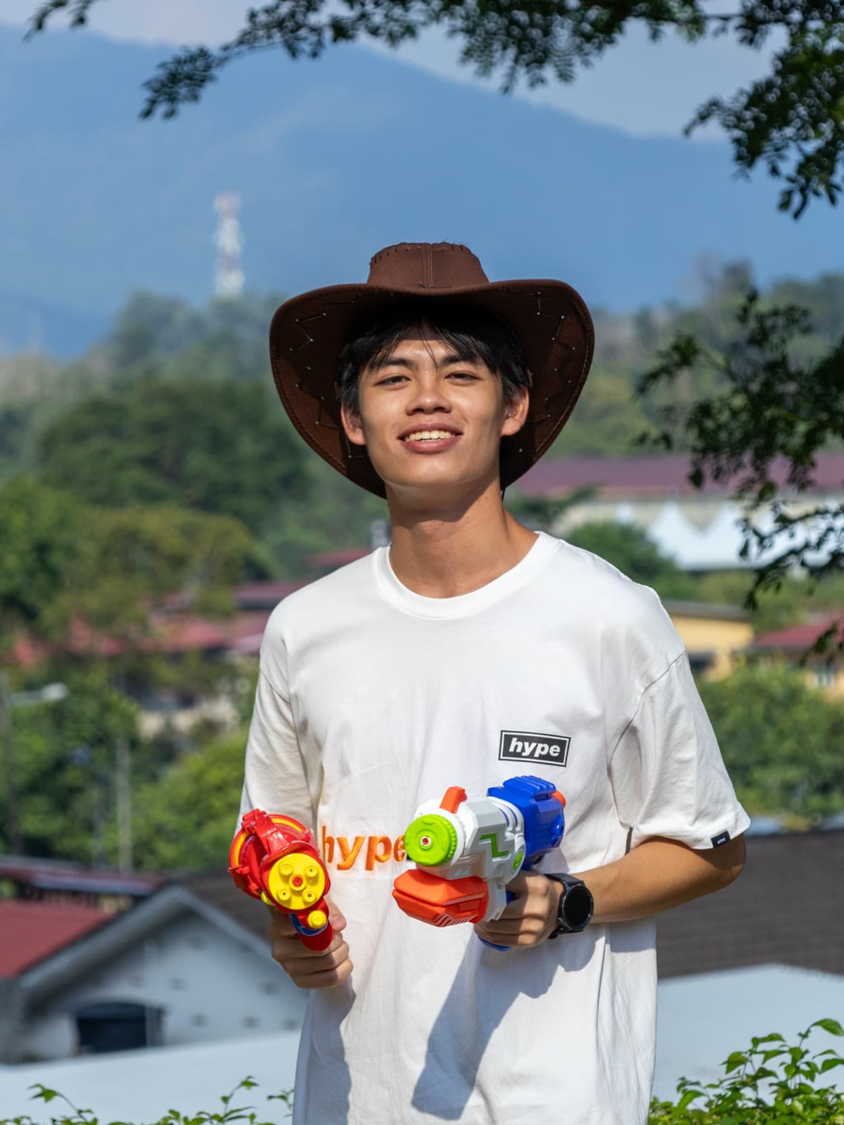 Joe, in a cowboy hat with two water guns, hills behind him